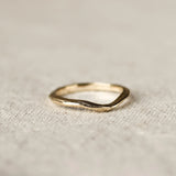 Gold ring with soft curve design and organic finishon a textured beige fabric background