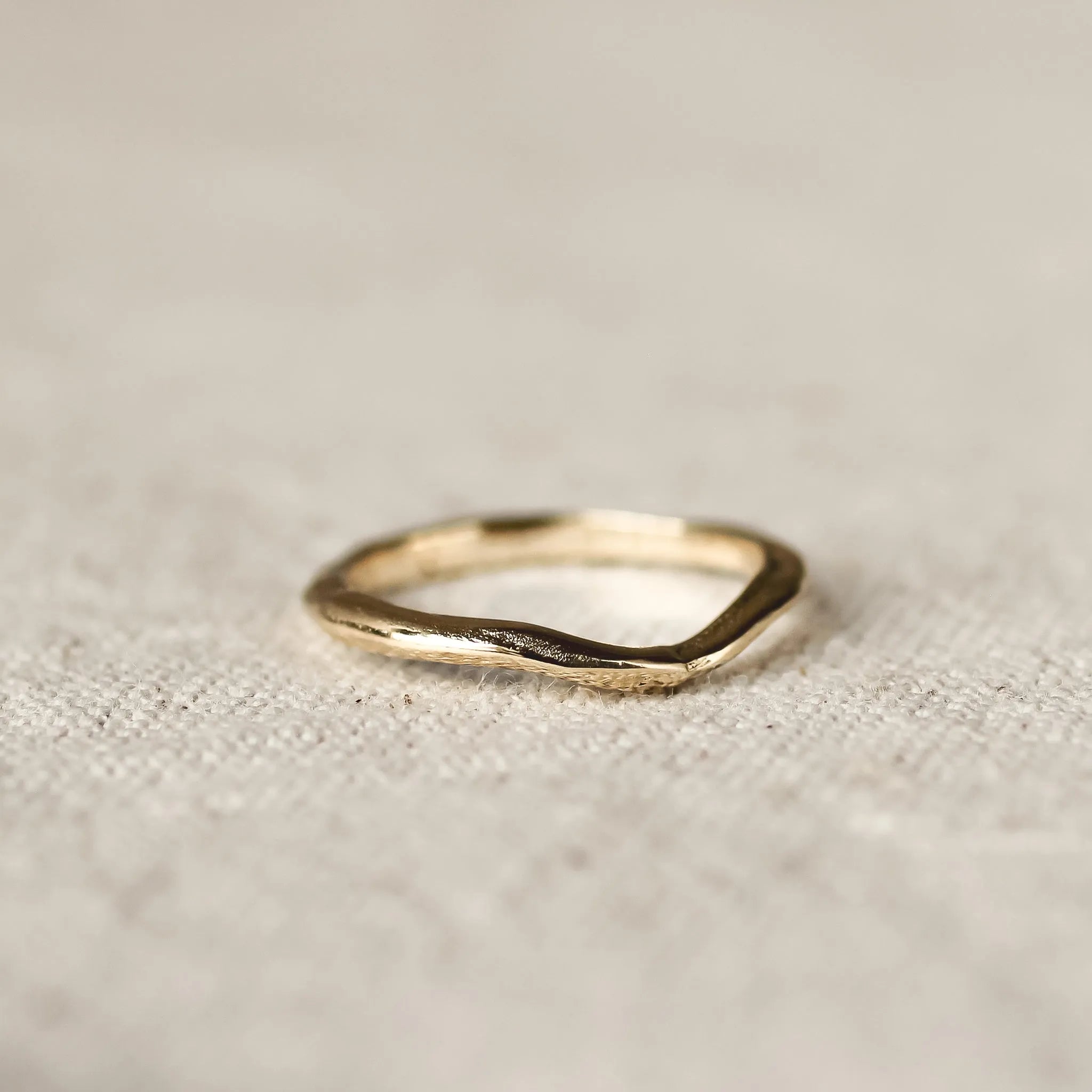 Gold ring with soft curve design and organic finishon a textured beige fabric background
