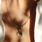 chunky gold necklace with a textured round pendant worn by a person in a white shirt, with shadows
