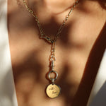 Gold chunky necklace with a round engraved pendant worn lariat style on a person wearing a white shirt.