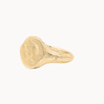 A textured gold signet ring with a chunky, organic shape, photographed on a clean off-white background.