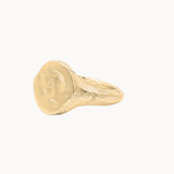 A textured gold signet ring with a chunky, organic shape, photographed on a clean off-white background.
