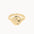 A textured gold signet ring with a rough, organic surface finish, shown on a plain off-white background.