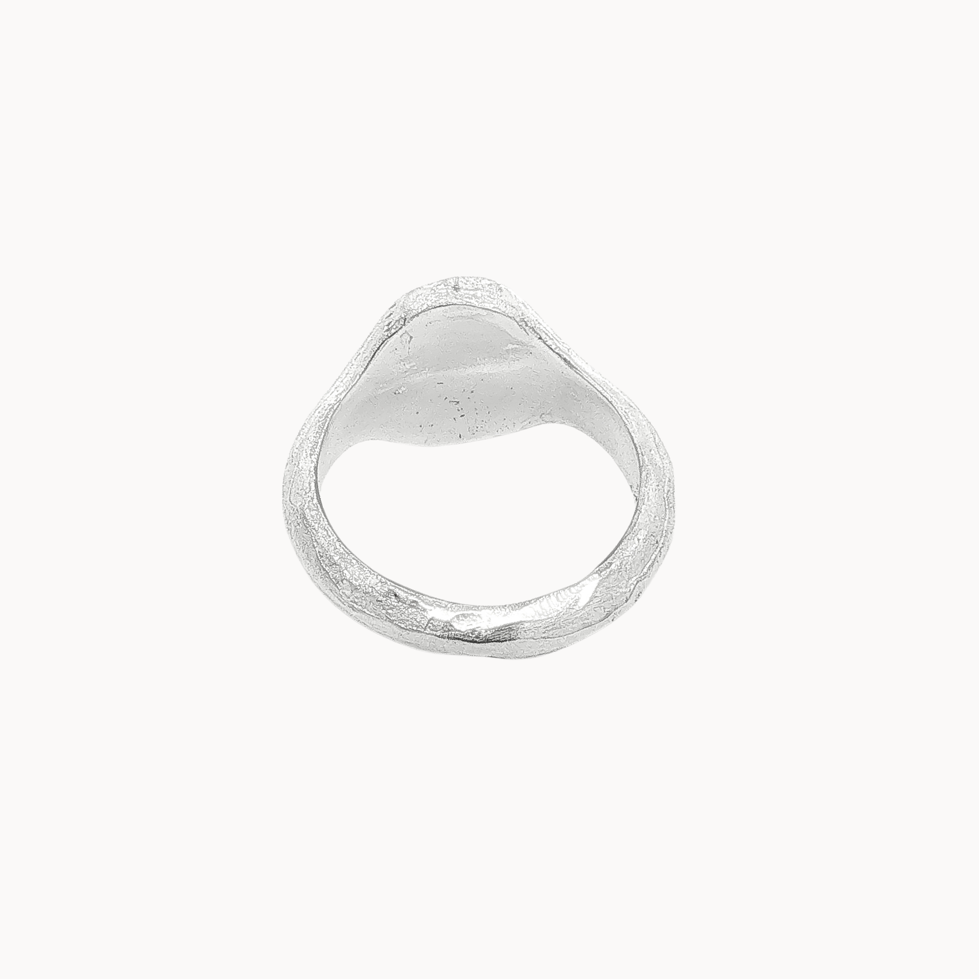 Back view of a textured silver signet ring with an oval face, photographed on a clean, solid off-white background.
