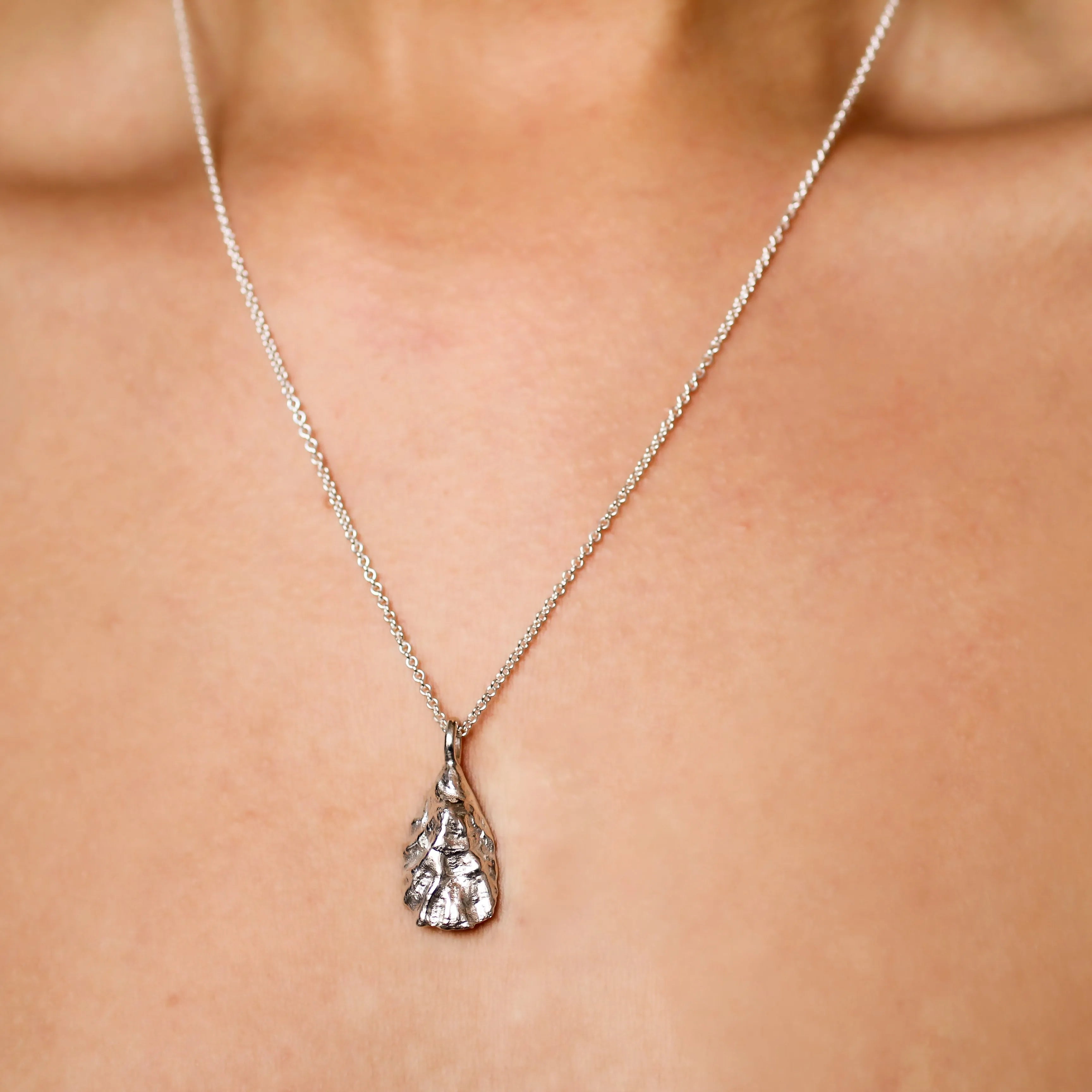 close up of oyster shell necklace on silver chain worn by model