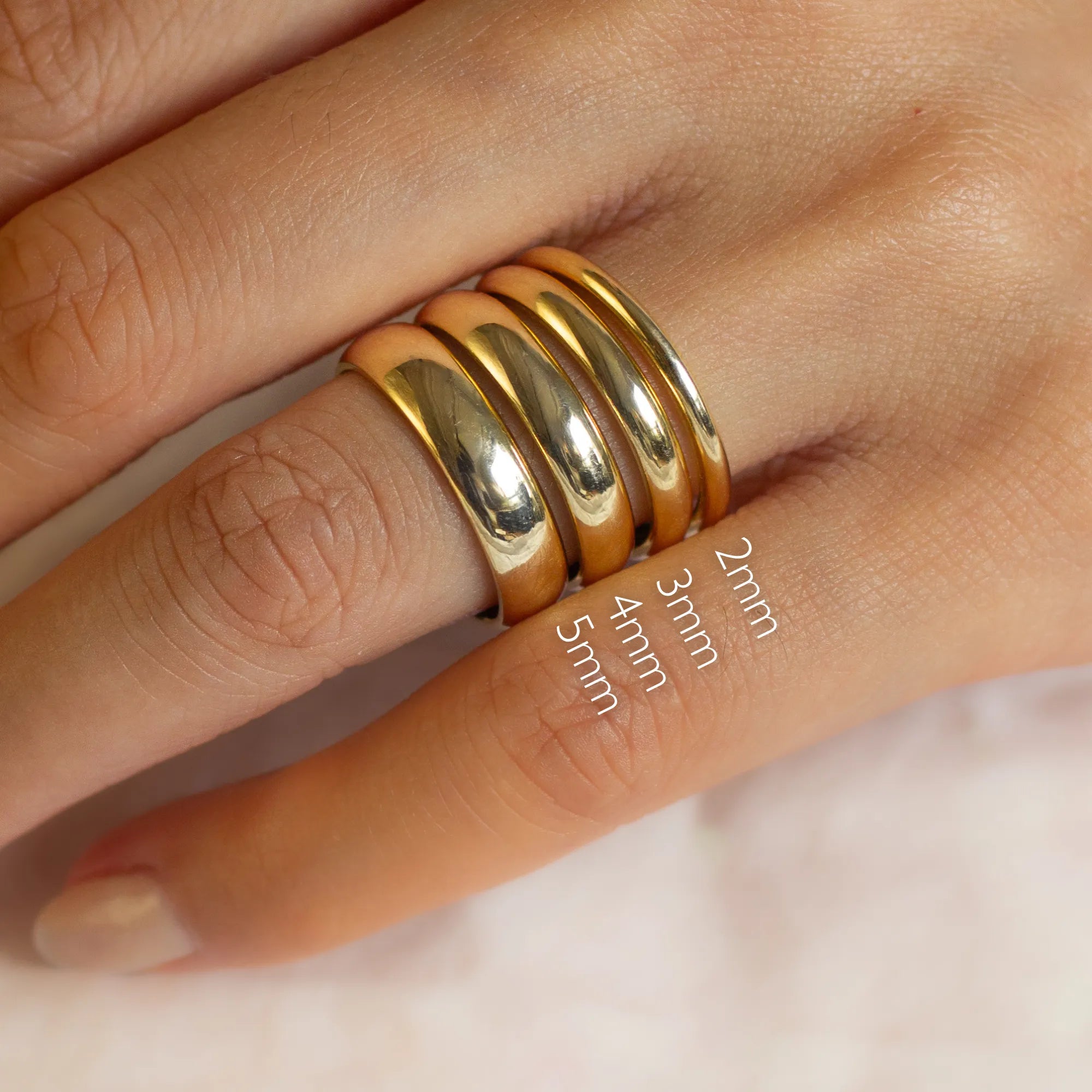 4 gold d shaped wedding rings on a finger with size labels 2mm, 3mm, 4mm and 5mm