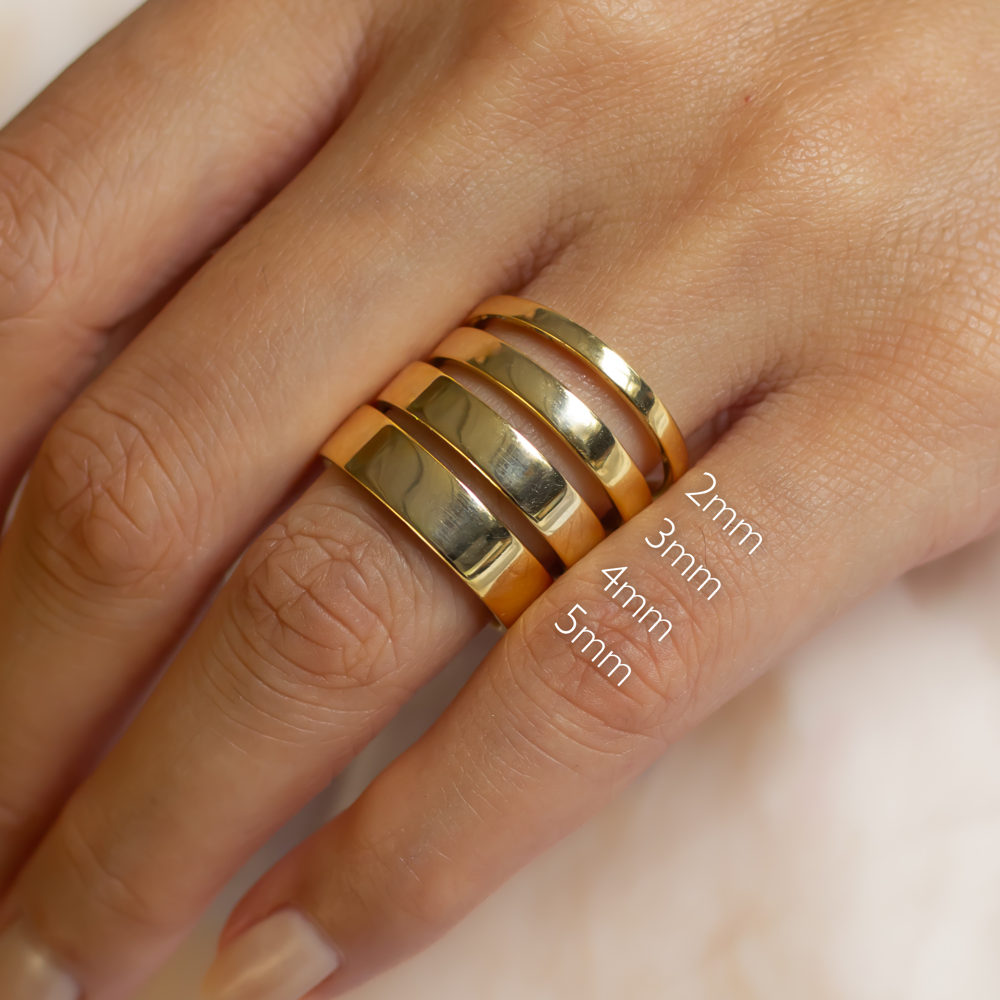 four gold flat wedding rings on a finger with size measurements: 2mm, 3mm, 4mm and 5mm