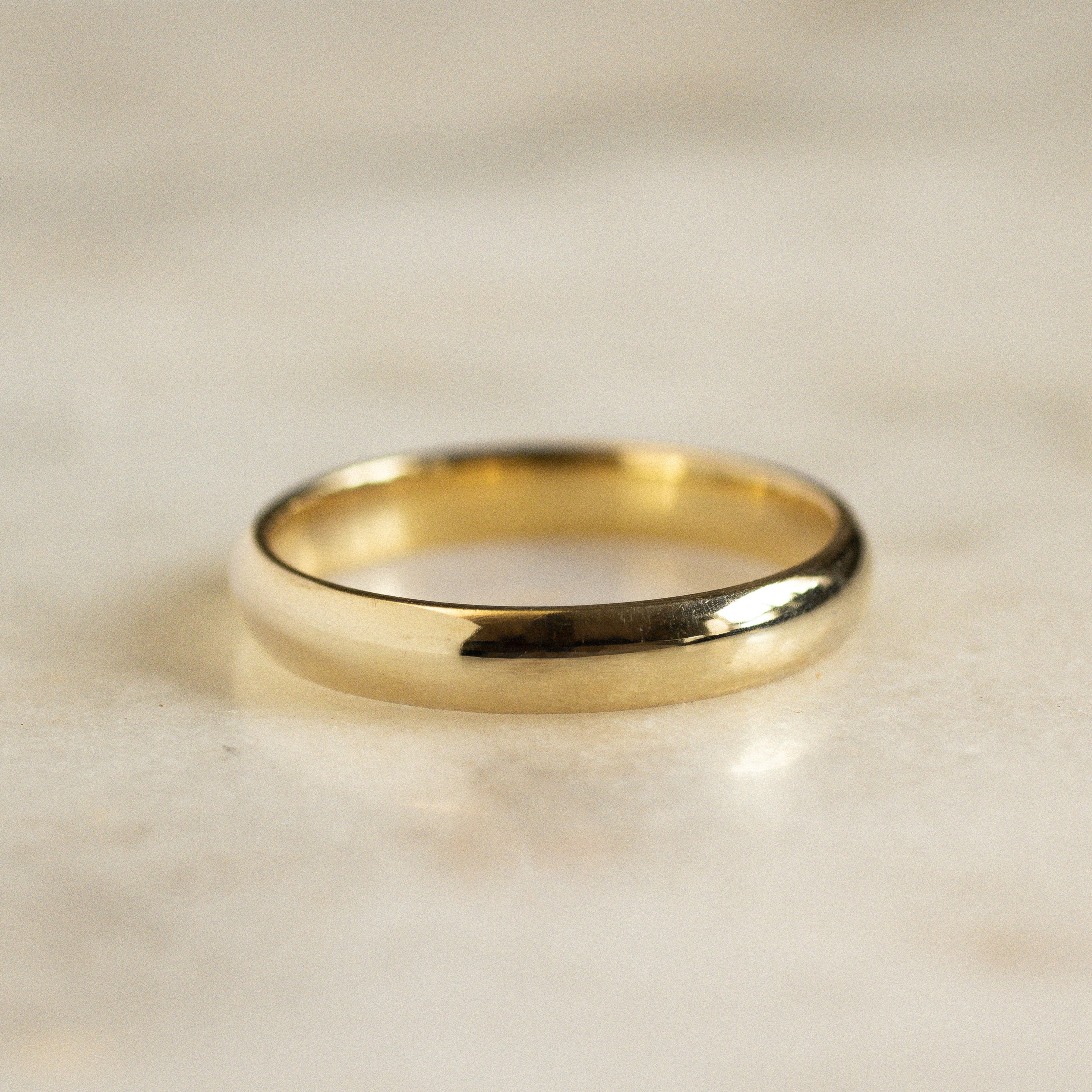 traditional d shaped gold wedding ring with high shine polished finish on marble surface