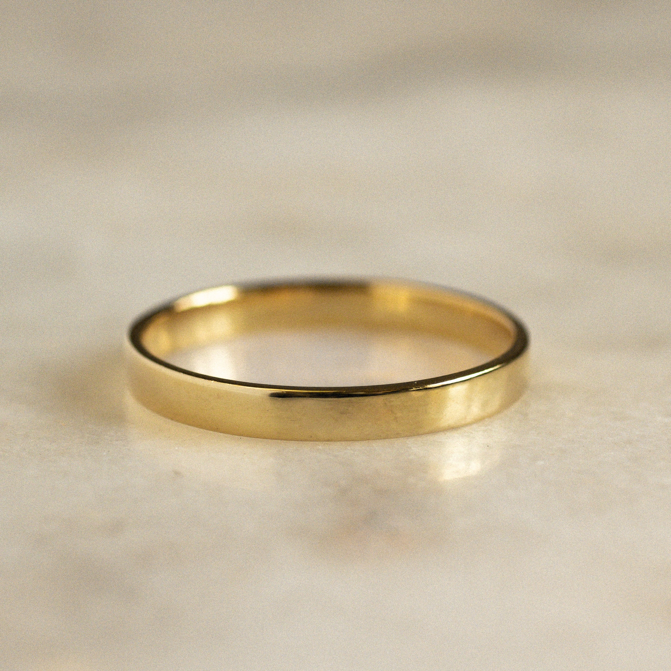 Gold flat wedding ring on a beige marble surface