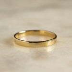 Gold flat wedding ring on a beige marble surface