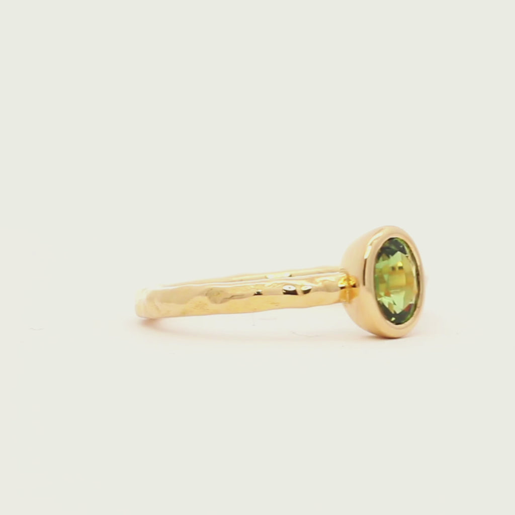 green bezel set engagement ring with textured band spinning on a turntable