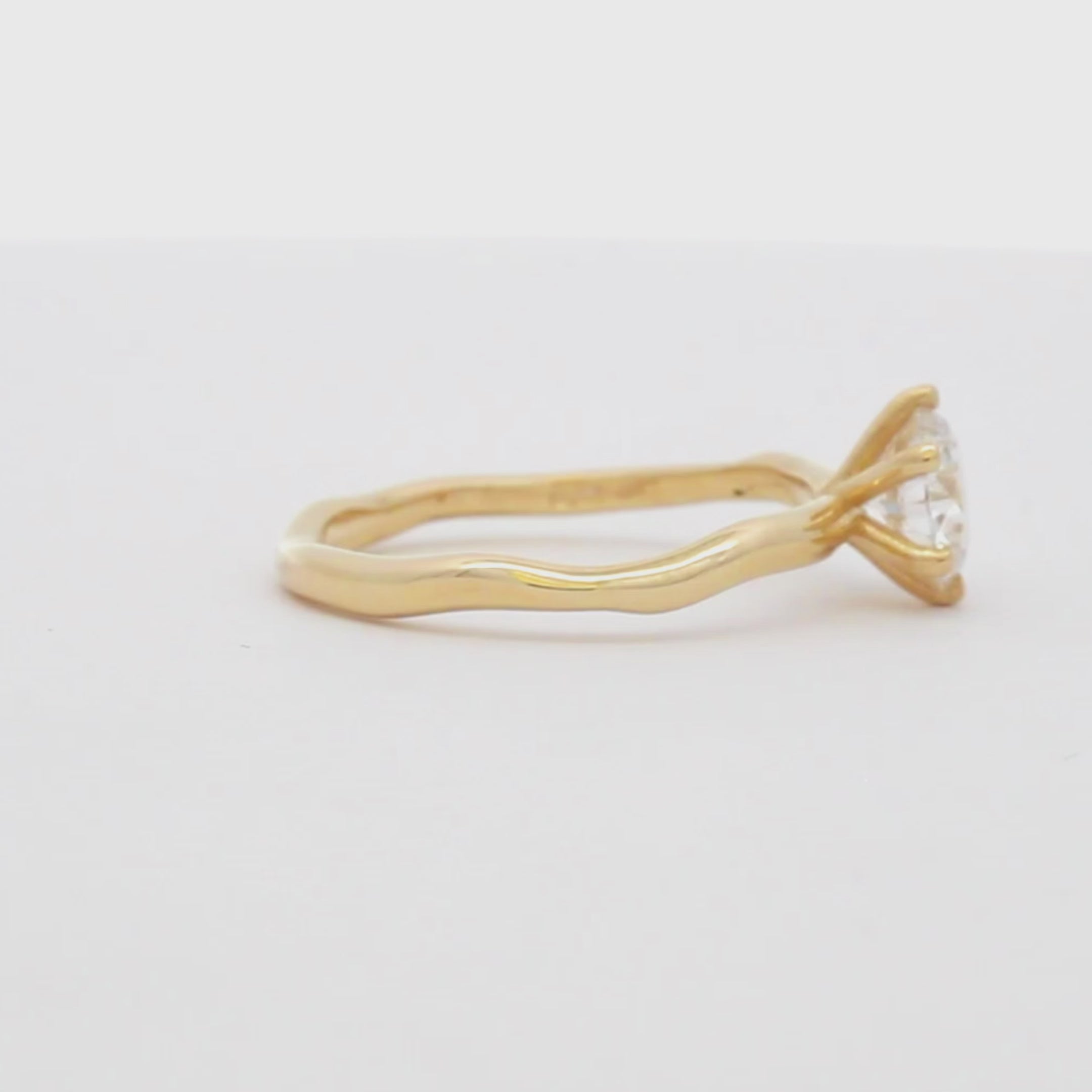 yellow gold solitaire engagement ring with round diamond and organic band spinning on a turntable