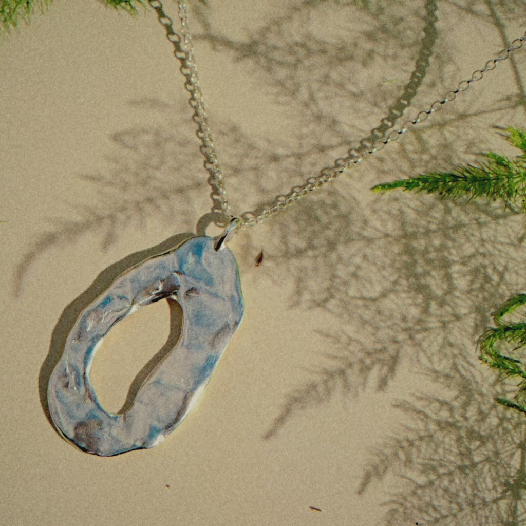 chunky oval necklace on a beige surface with shadows of a plant moving