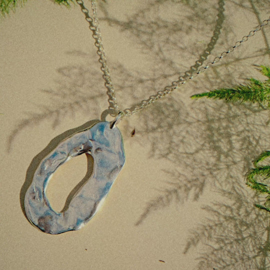chunky oval necklace on a beige surface with shadows of a plant moving