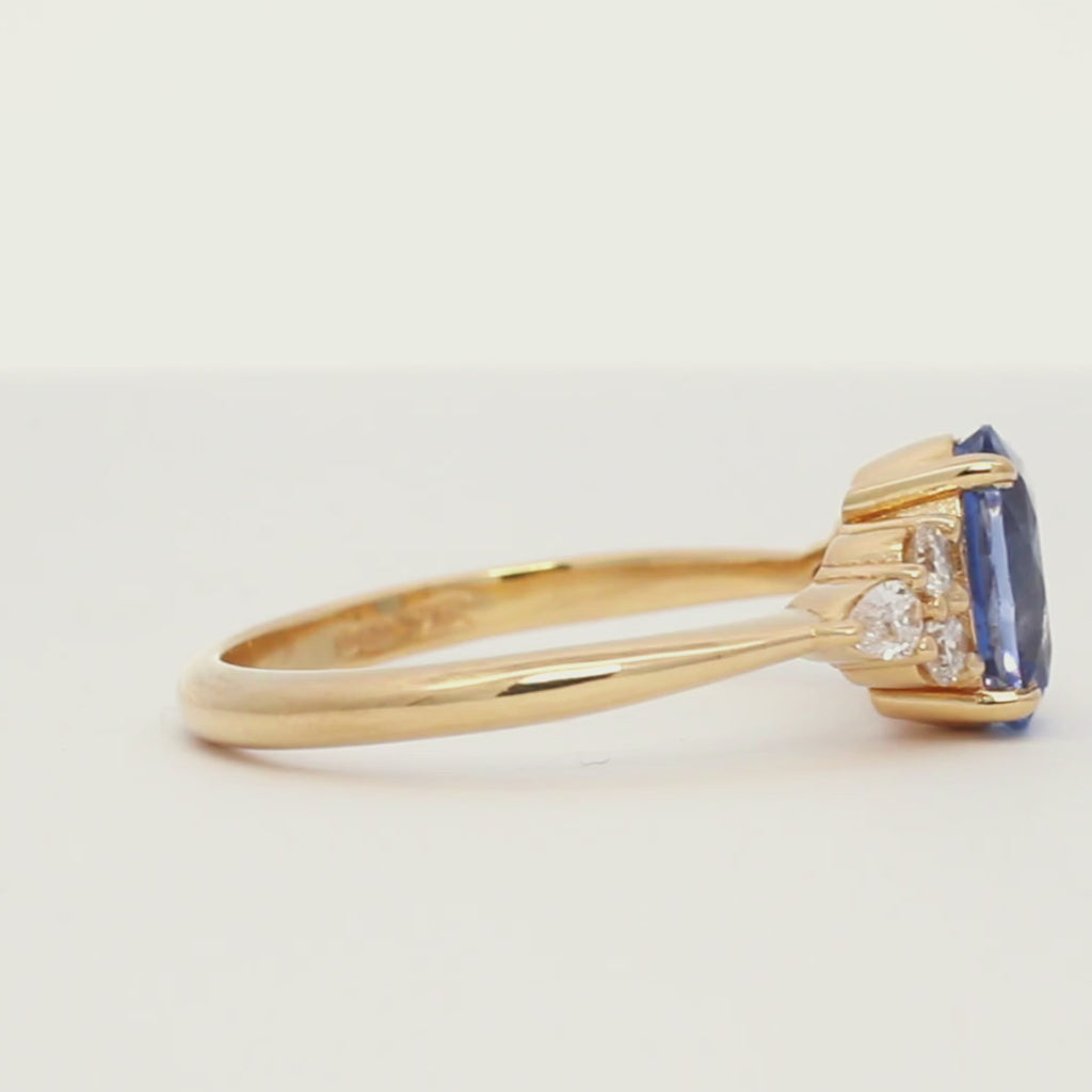 cornflower blue oval sapphire engagement ring with diamond cluster spinning on a turntable