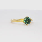 solitaire yellow gold engagement ring with greeny blue round sapphire and wavy organic band spinning on a turntable