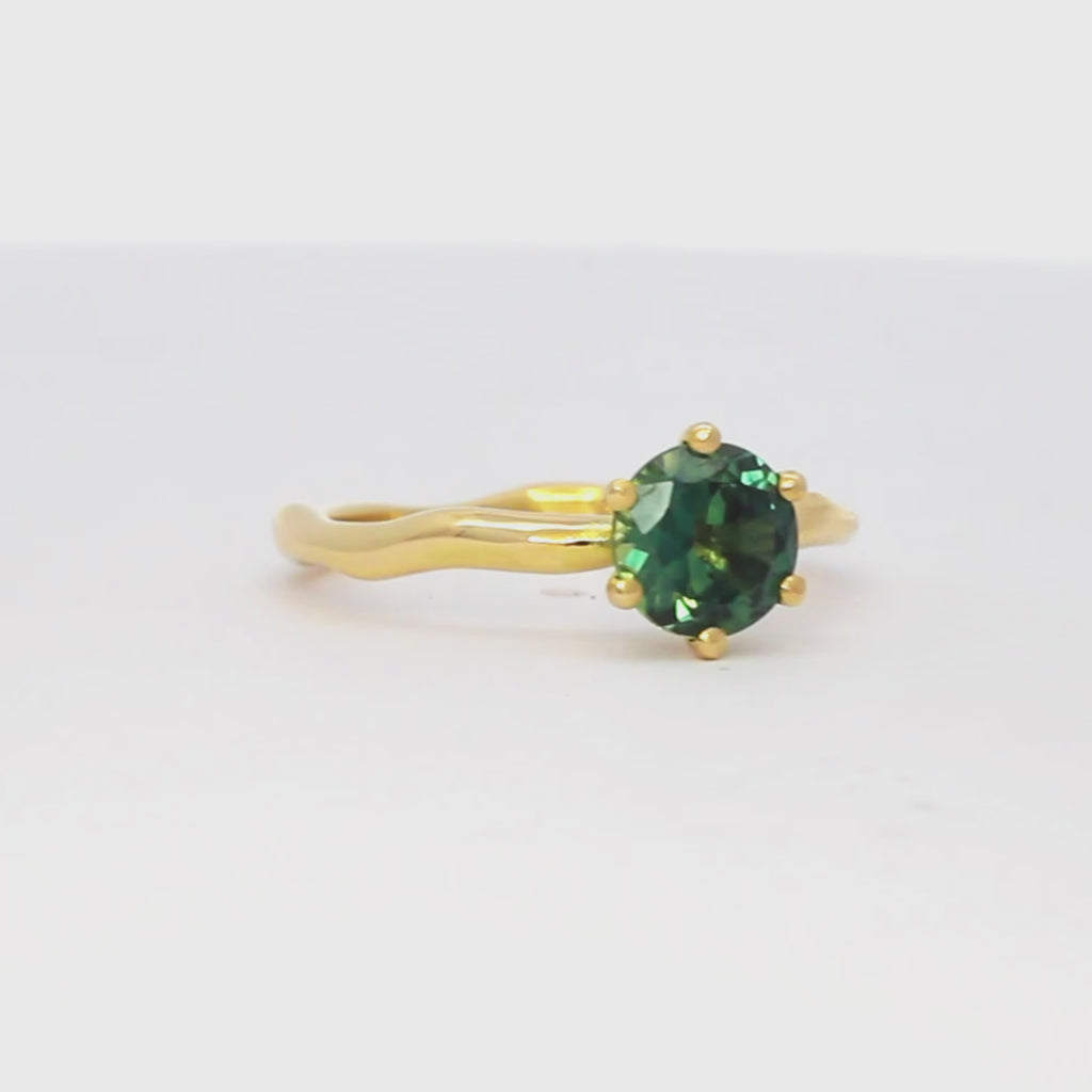 solitaire yellow gold engagement ring with greeny blue round sapphire and wavy organic band spinning on a turntable
