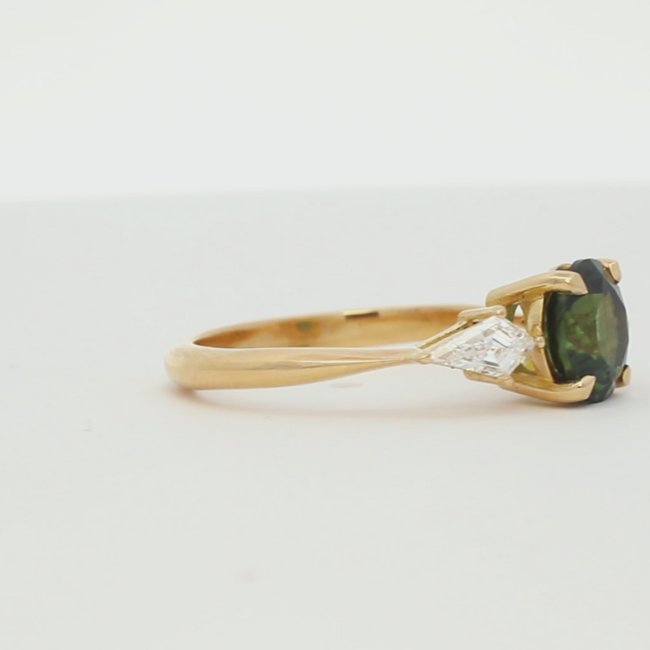 green sapphire engagement ring with round centre stone and kite shaped diamonds spinning on a turntable