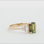 gold engagement ring with green emerald-cut sapphire and diamond cluster spinning on a turntable