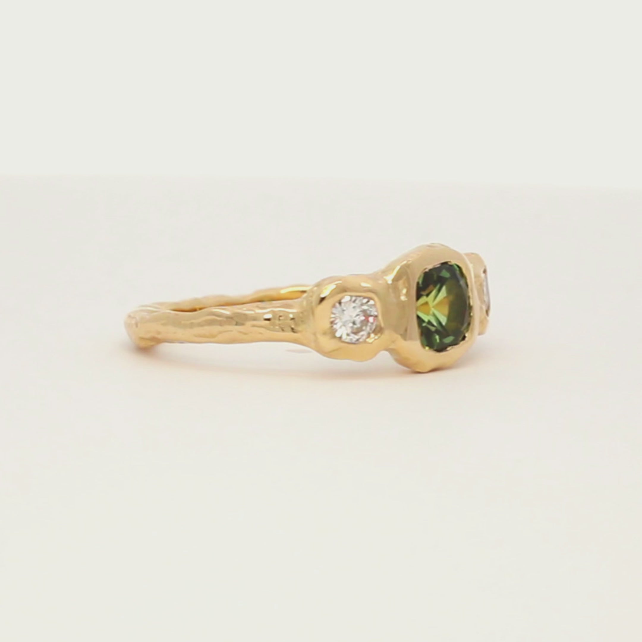 cushion cut green sapphire trilogy engagement ring with molten organic texture spinning on a turntable