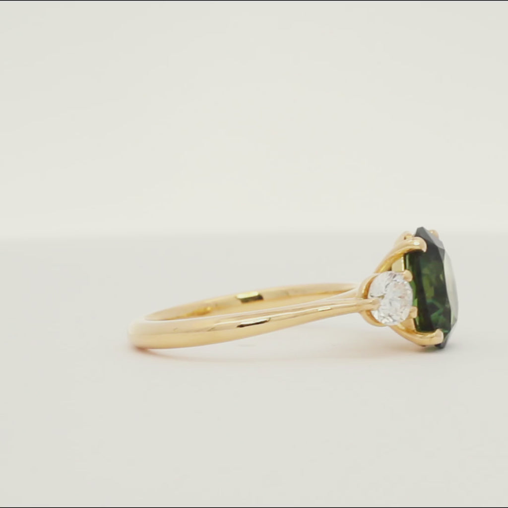 large sapphire engagement ring with green stone and smaller diamonds spinning on a turntable