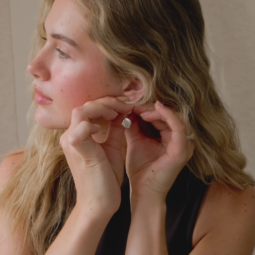 close up of model putting in silver pebble dangle earrings and tucking her hair behind her ear