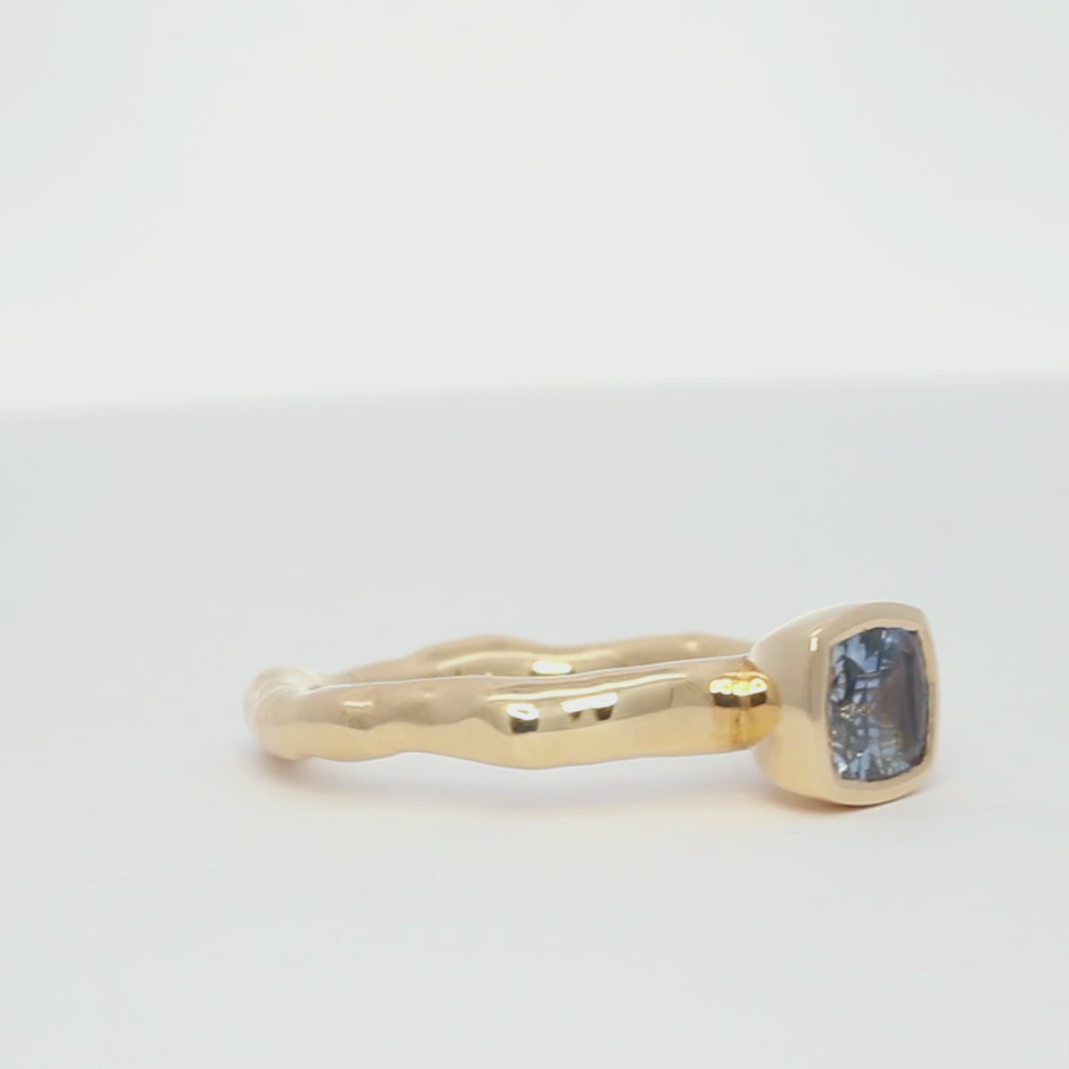 sky blue east-west sapphire bezel engagement ring with molten band spinning on a turntable with a white background