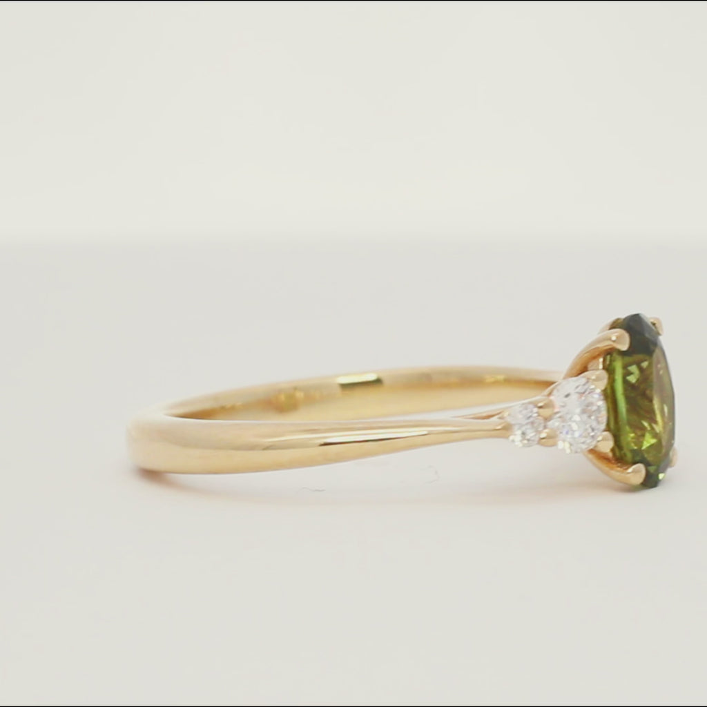 gold engagement ring with green sapphire and four tapered accent diamonds spinning on a turntable