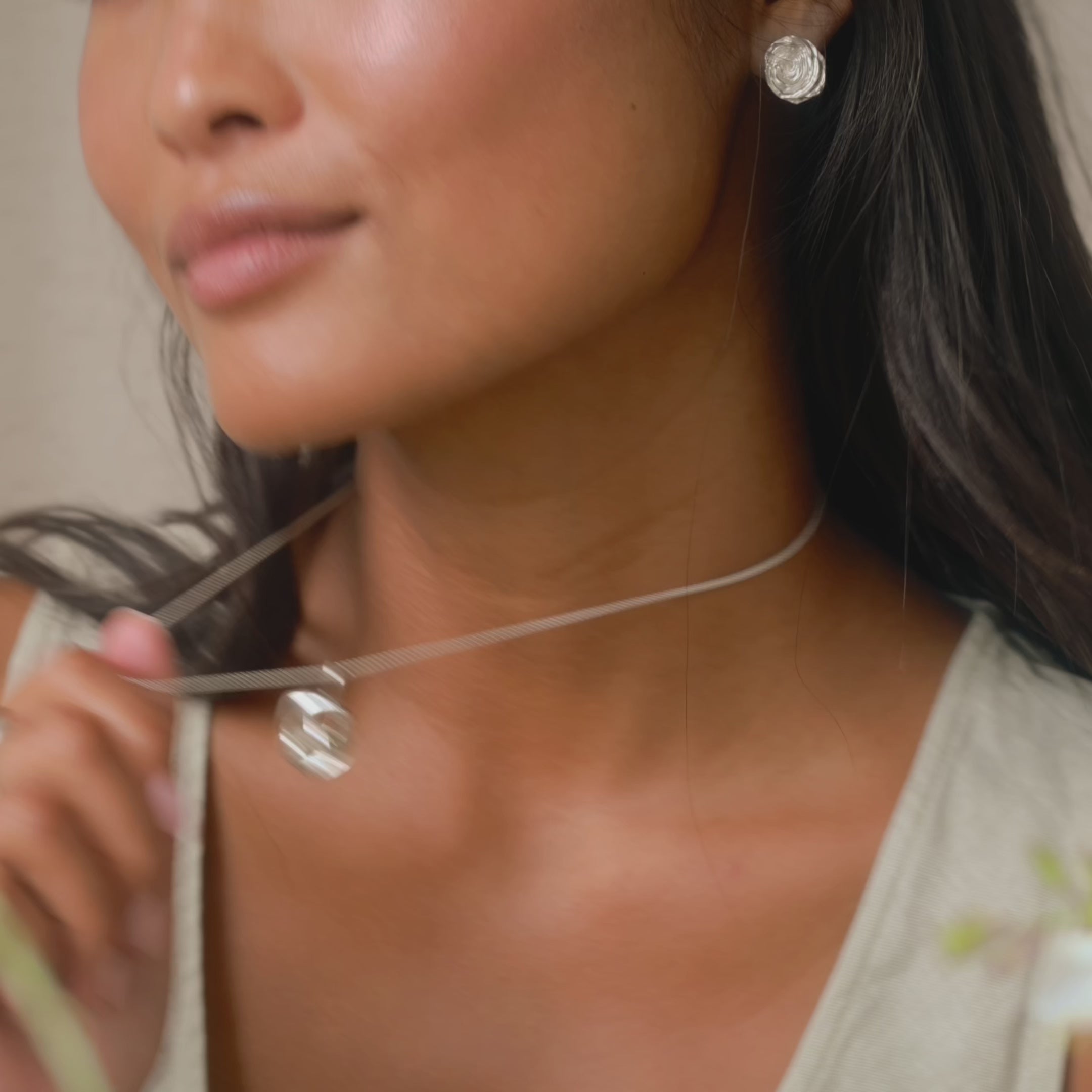 model playing with chunky silver necklace with large knot pendant, and wearing silver stud earrings smiling to camera