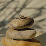 chunky silver knot ring on top of pebbles with shadows and a rainbow light reflecting