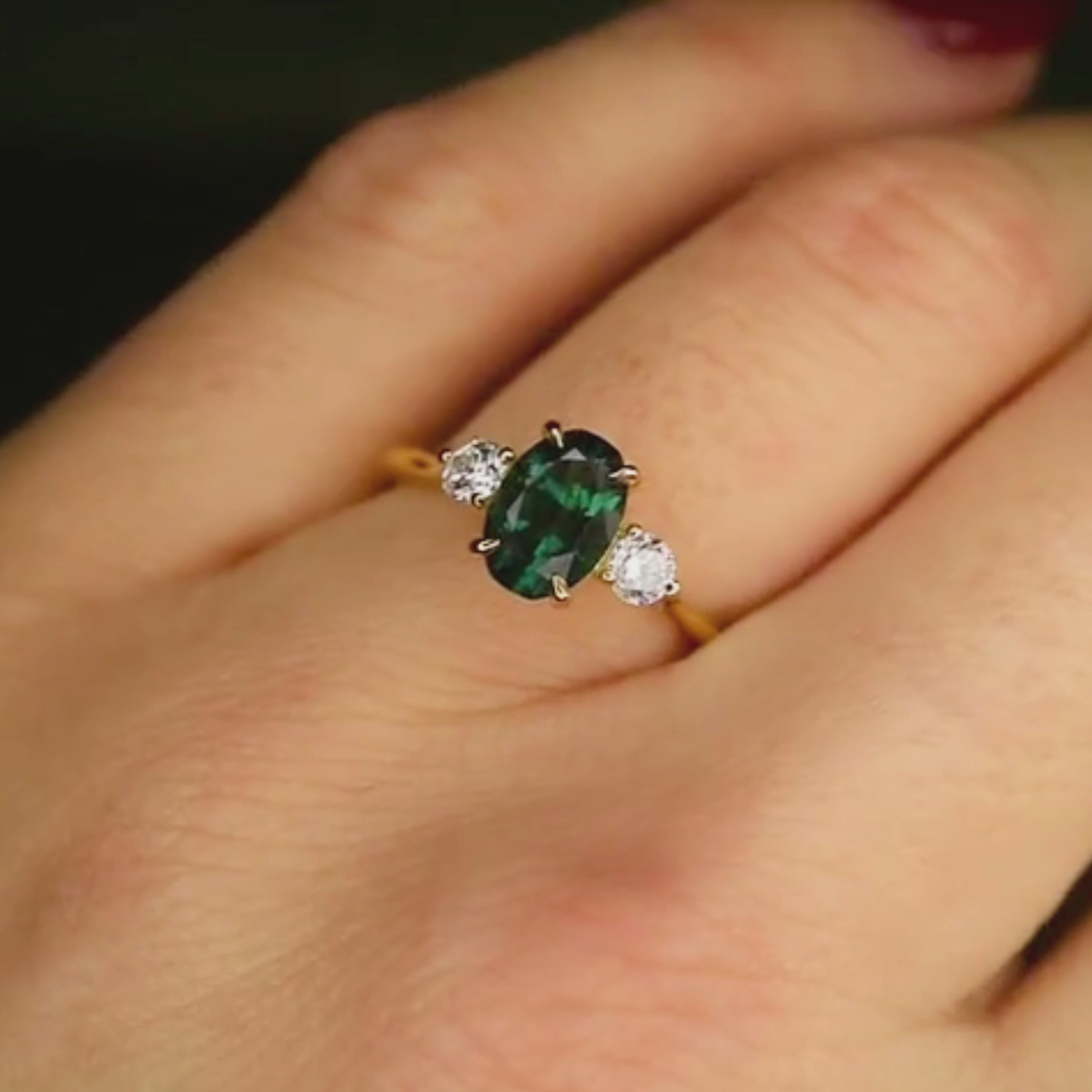 oval bi-colour blue green engagement ring with round diamonds worn on finger in the light