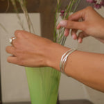 hands arranging flowers in a green vase, wearing a silver chunky ring and open silver bangle
