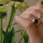hand wearing chunky thick band silver ring with a cabacon brown smoky quartz stone with flowers in the background