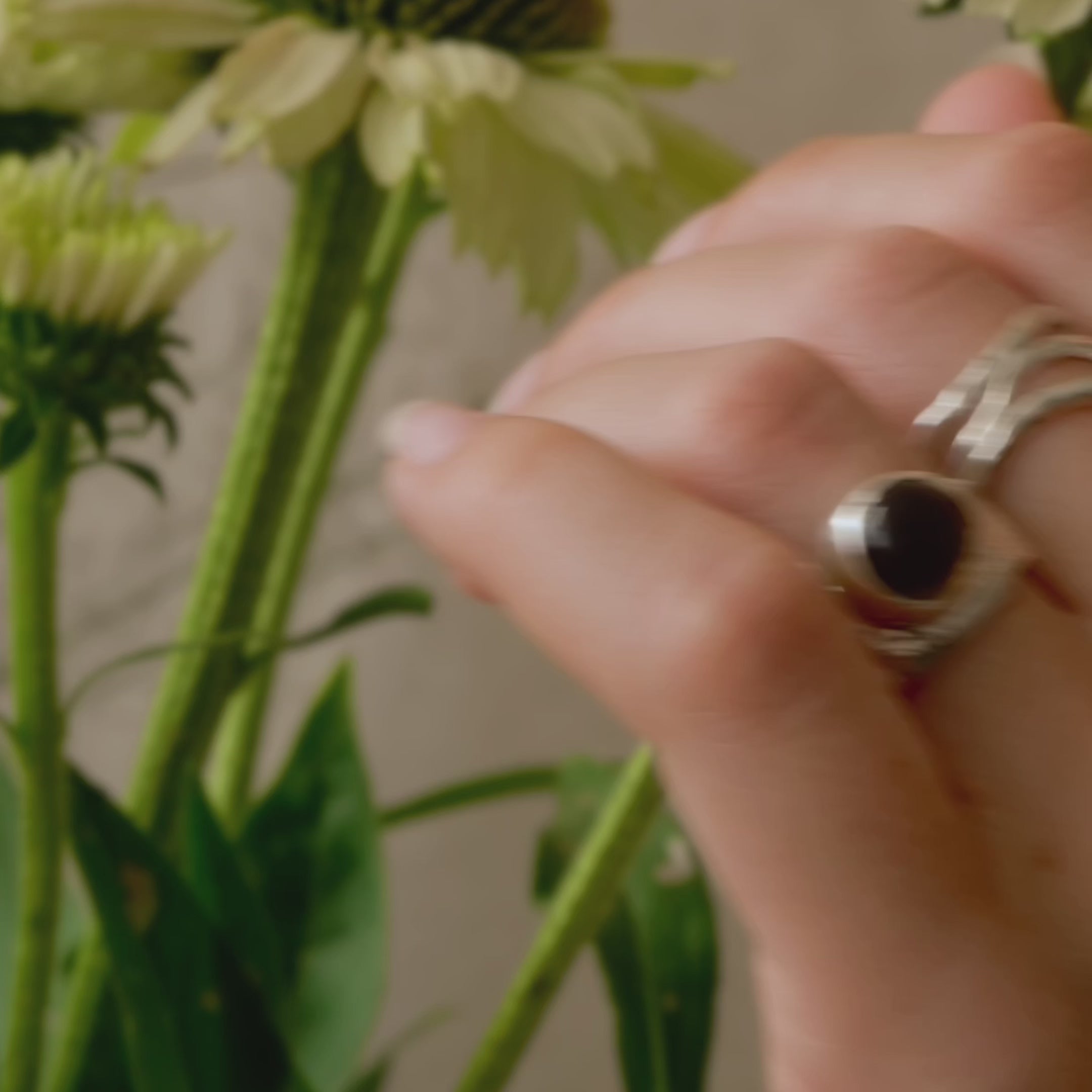 hand wearing chunky thick band silver ring with a cabacon brown smoky quartz stone with flowers in the background