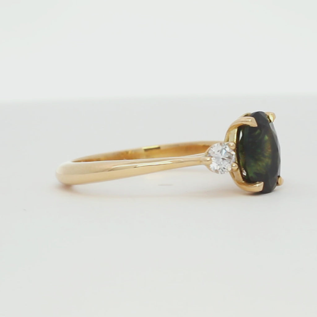 green stone engagement ring with oval sapphire and round diamonds spinning on a turntable