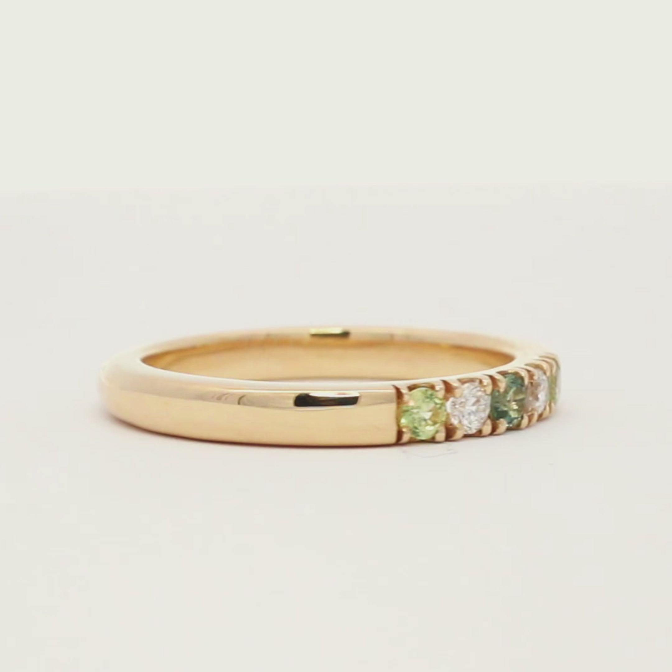 gold band ring with diamonds and green blue sapphires spinning on a turntable