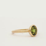 bezel set satin engagement ring with green yellow sapphire spinning on a turntable