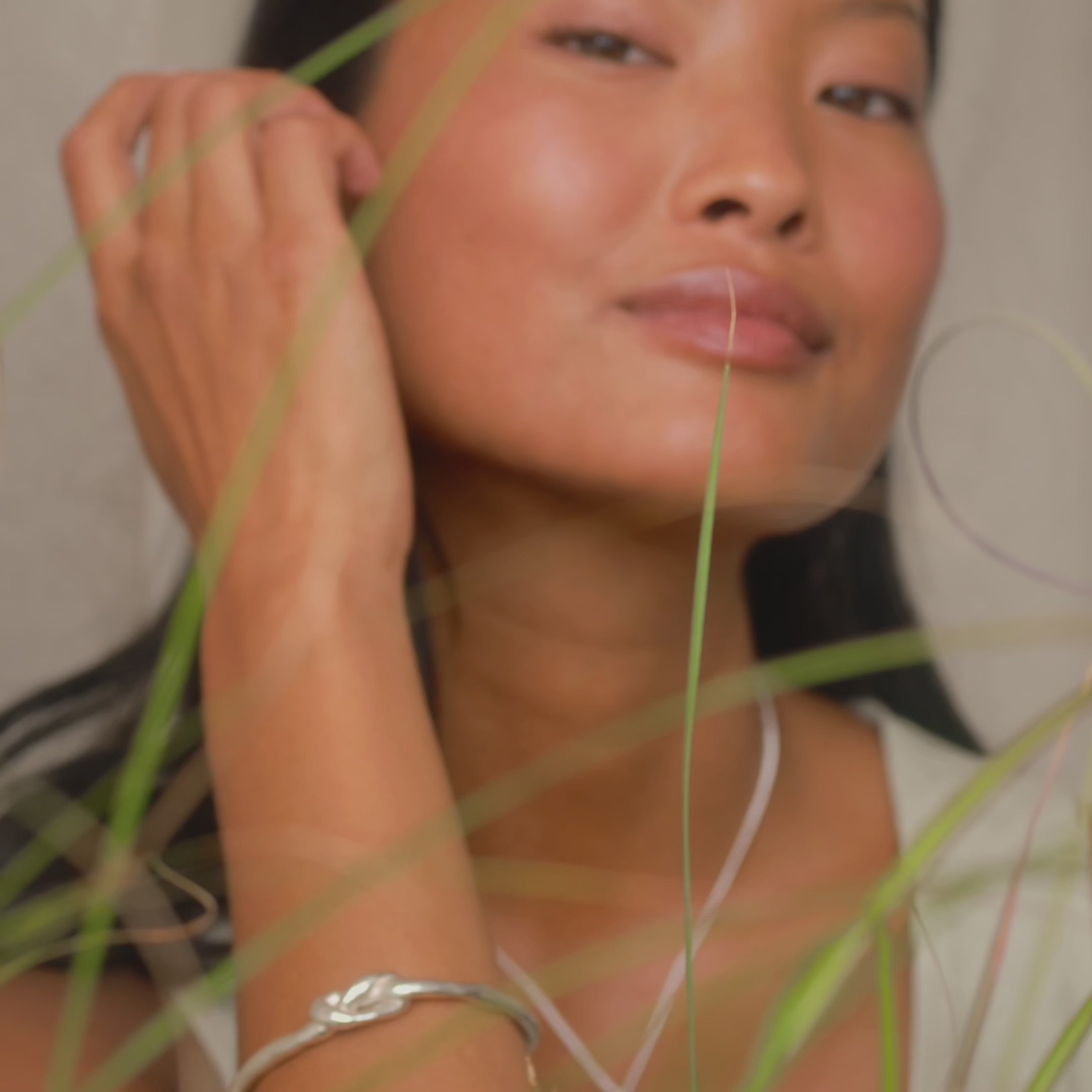 model tucking her hair behind her ear and leaning on her hand, wearing silver jewellery including knotted bangle and round studs