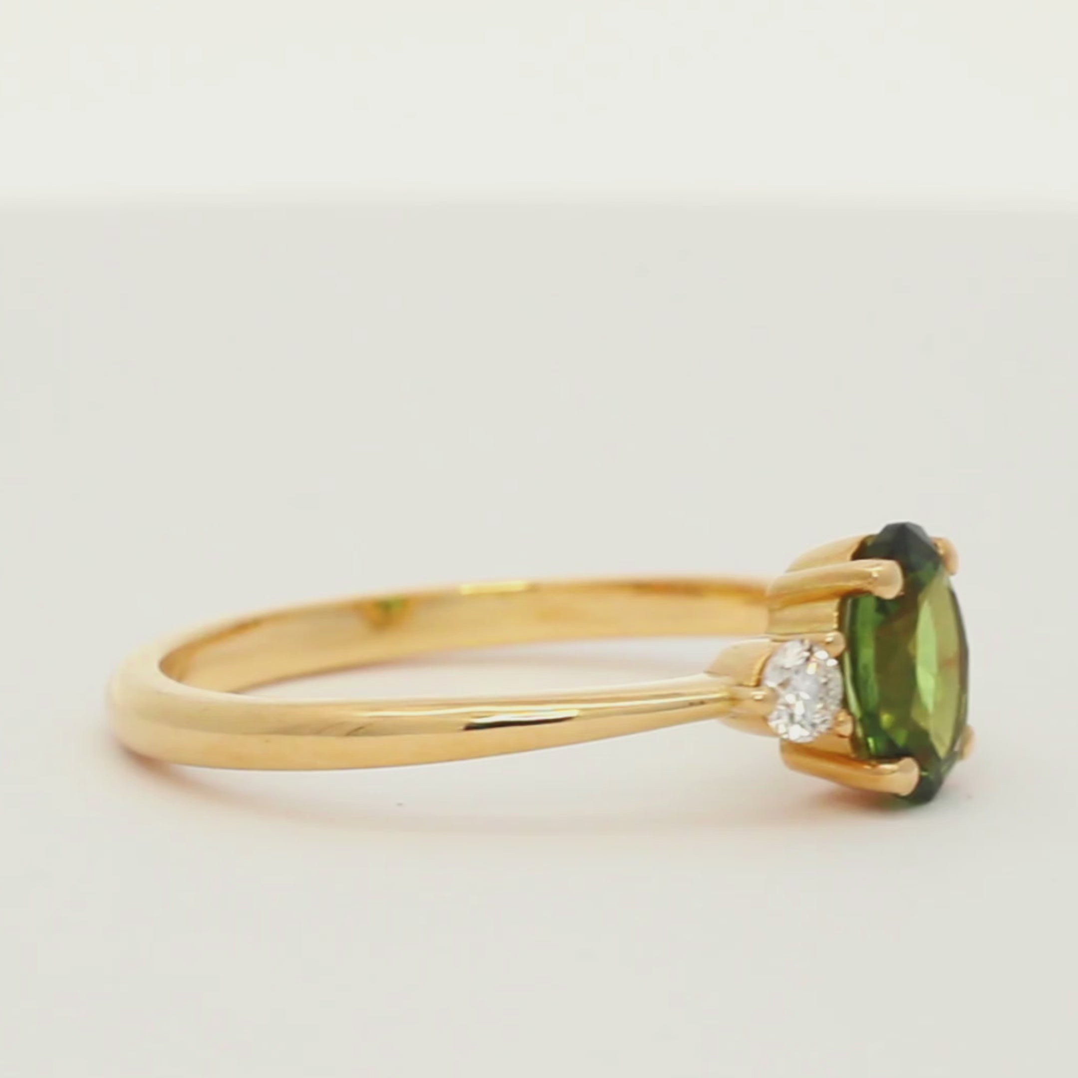 gold engagement ring with green oval sapphire and smaller diamonds spinning on a turntable