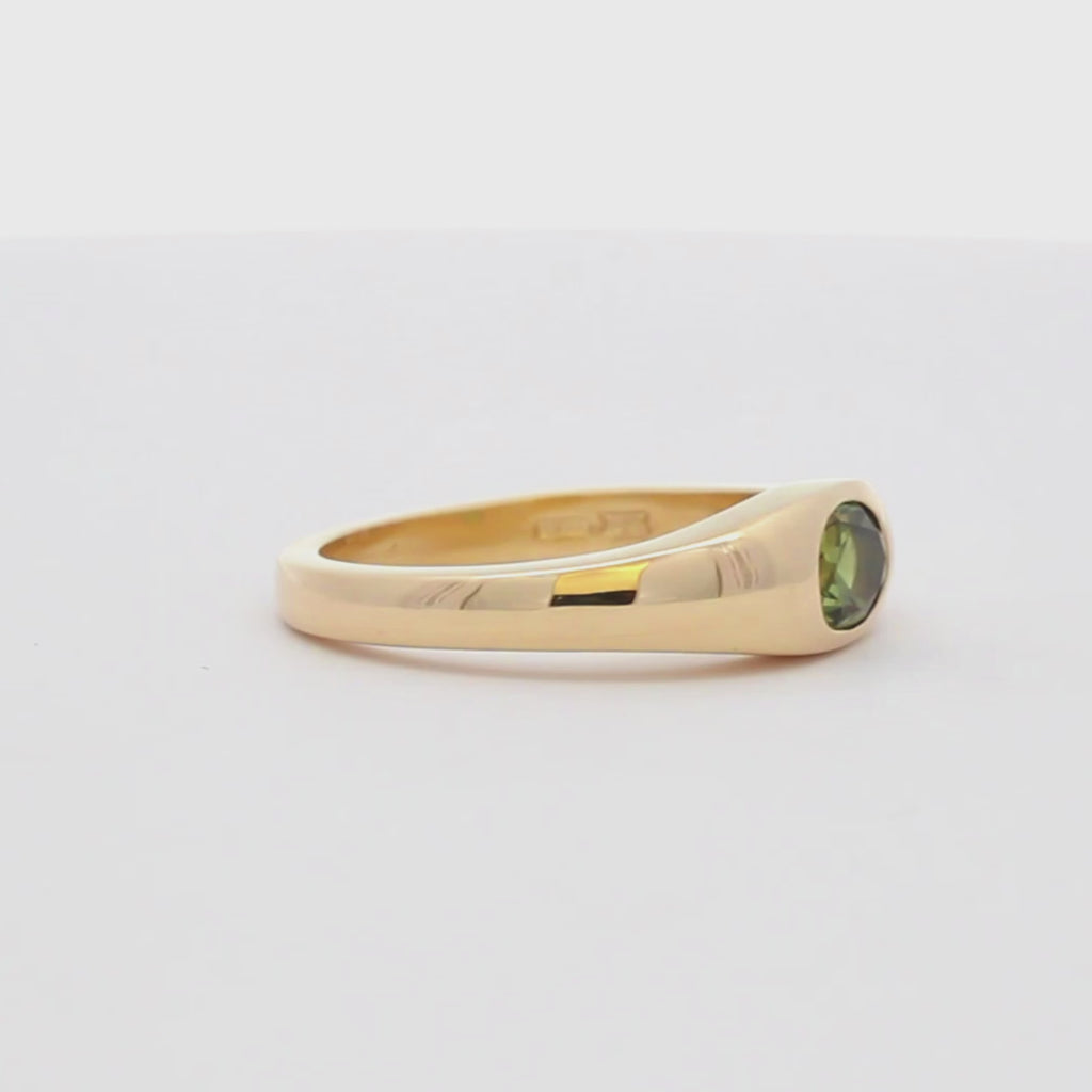 yellow gold band ring with oval green sapphire spinning on a turntable