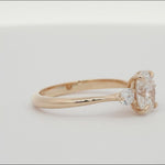 three diamond oval and round trilogy engagement ring spinning on a turntable