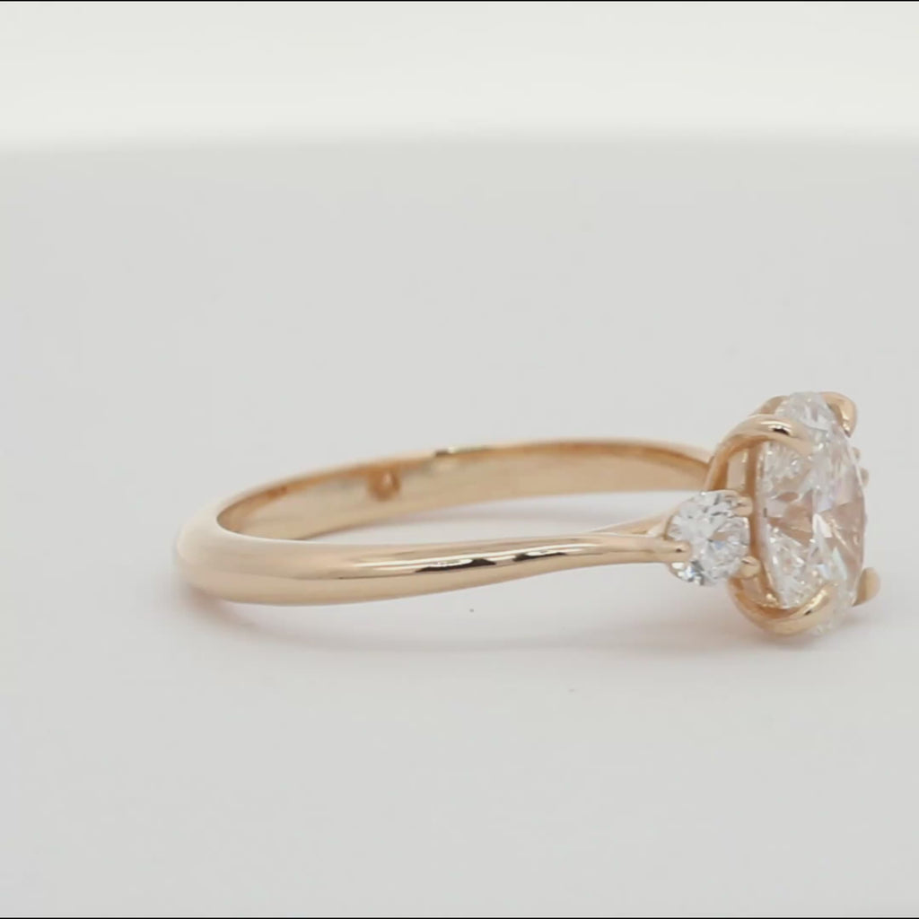 three diamond oval and round trilogy engagement ring spinning on a turntable