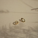 gold oval studs with molten texture on a beige surface with moving plant shadows