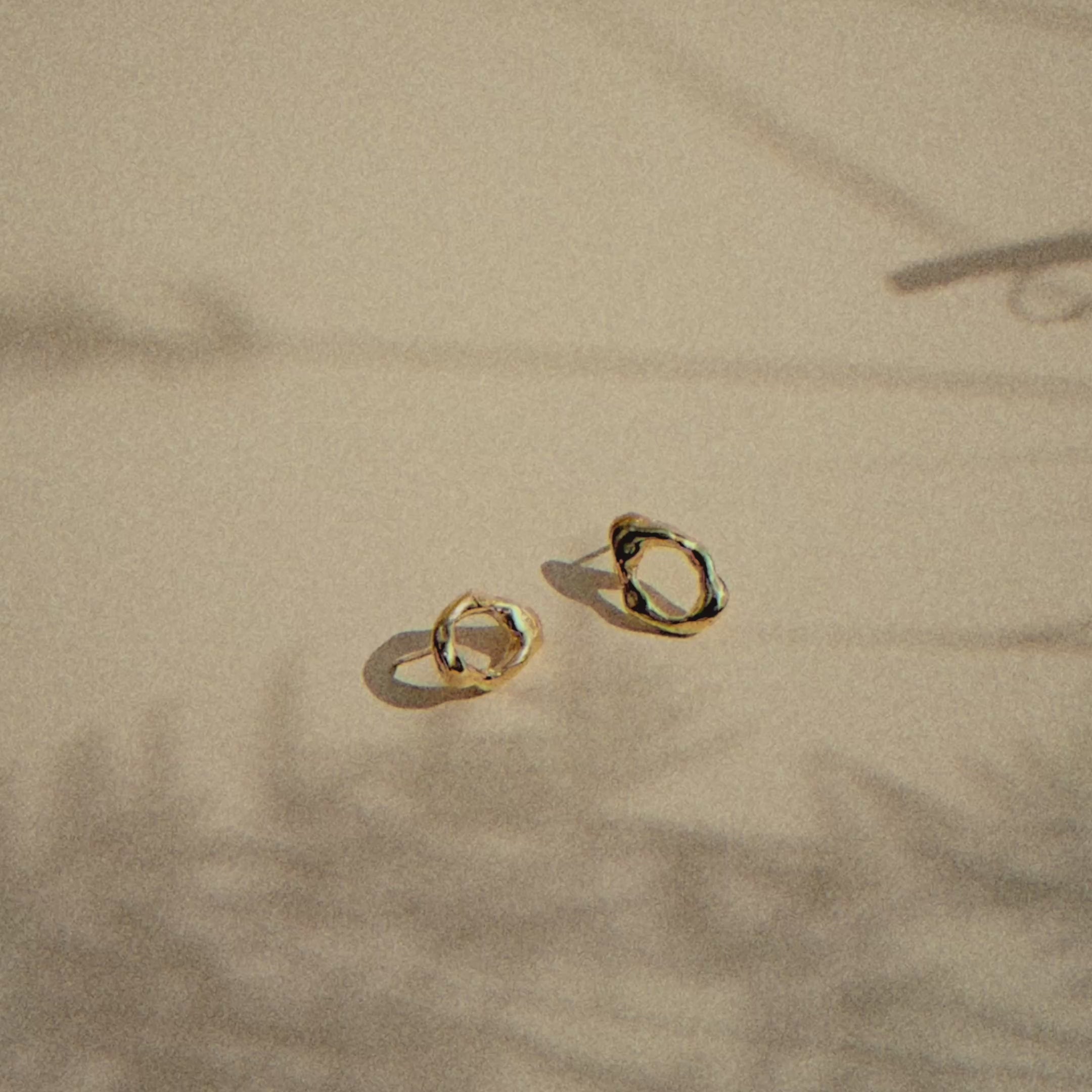 gold oval studs with molten texture on a beige surface with moving plant shadows