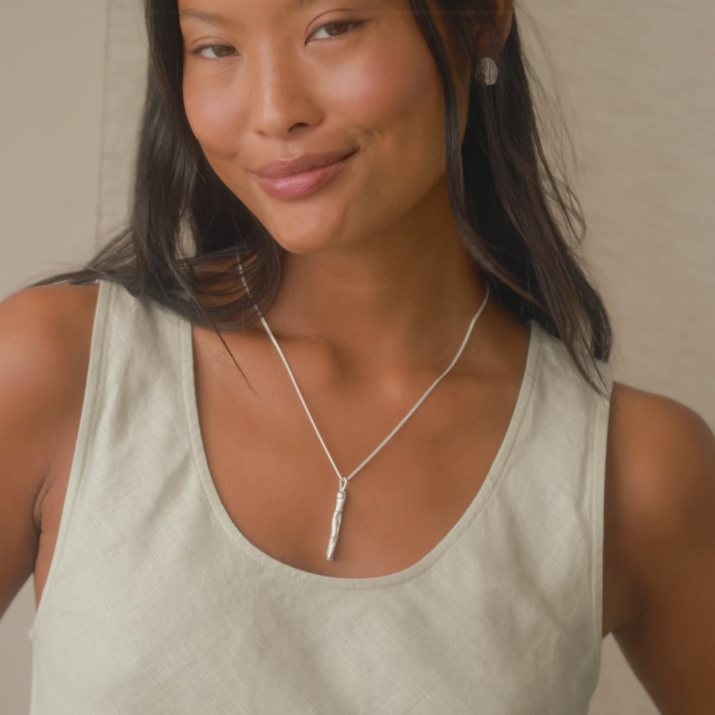 model wearing silver jewellery, including the entwined bar necklace with textured vertical pendant, playing with it and smiling to camera