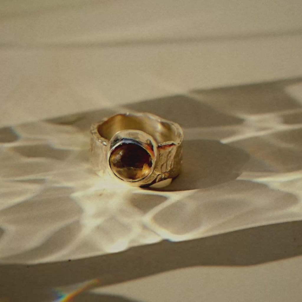 chunky silver ring with smoky quartz stone on a surface with water reflection