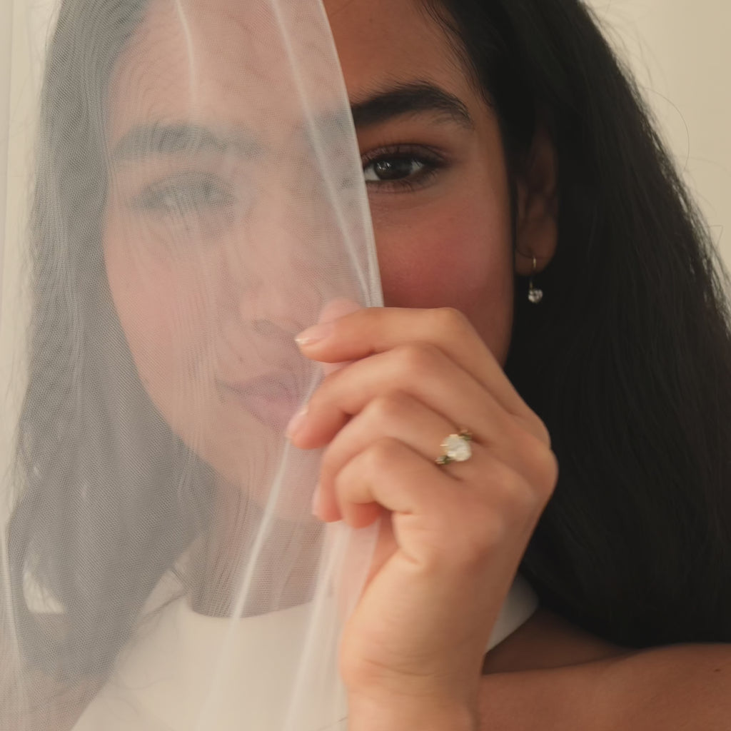 bride with black hair wearing engagement ring and diamond earrings posing behind a veil