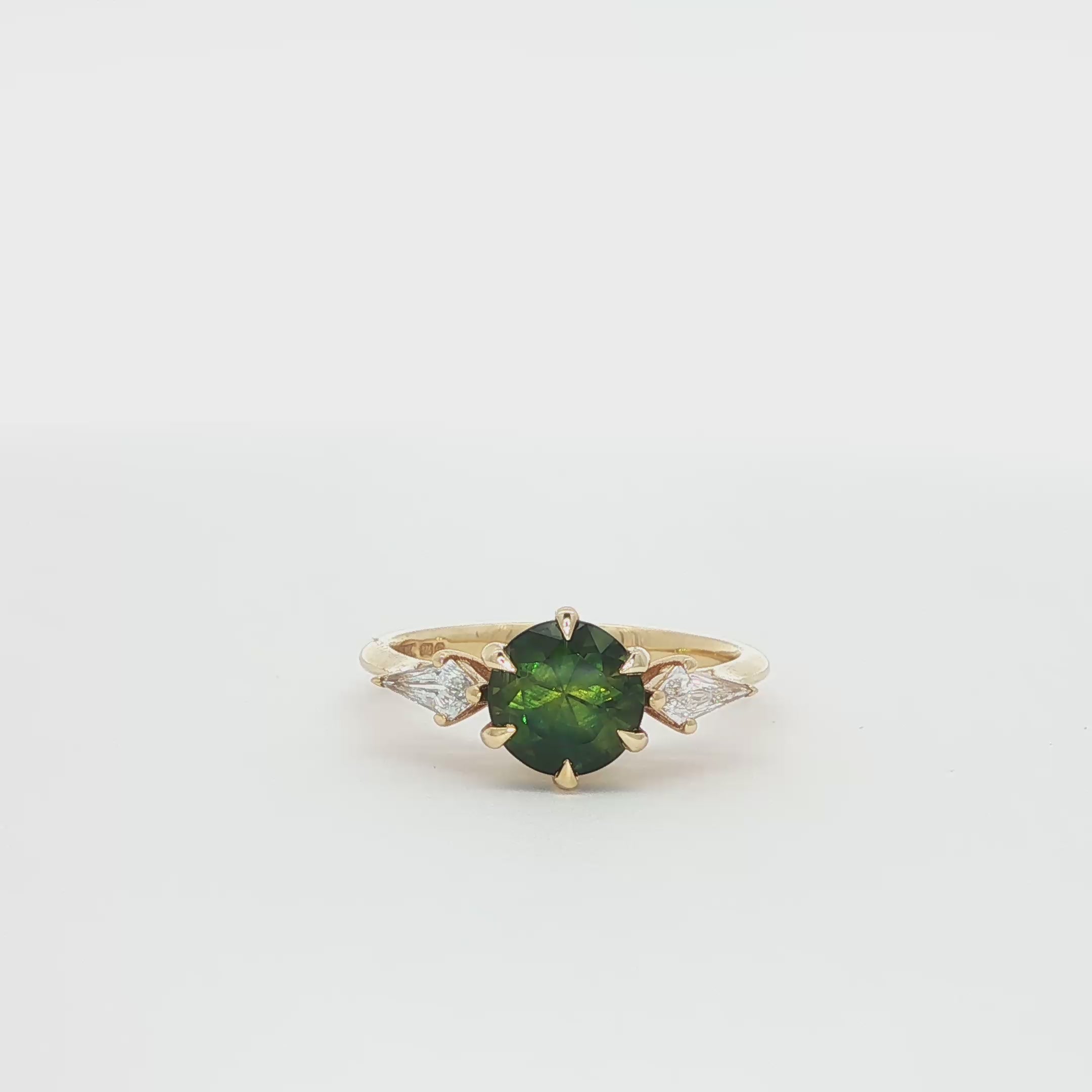 Dark green sapphire engagement ring with kite diamonds on a spinning turntable