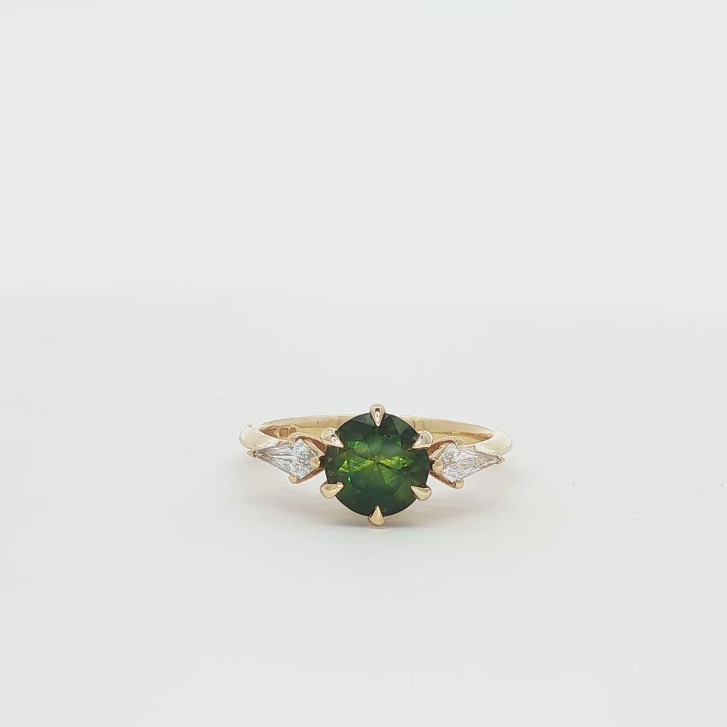 Dark green sapphire engagement ring with kite diamonds on a spinning turntable