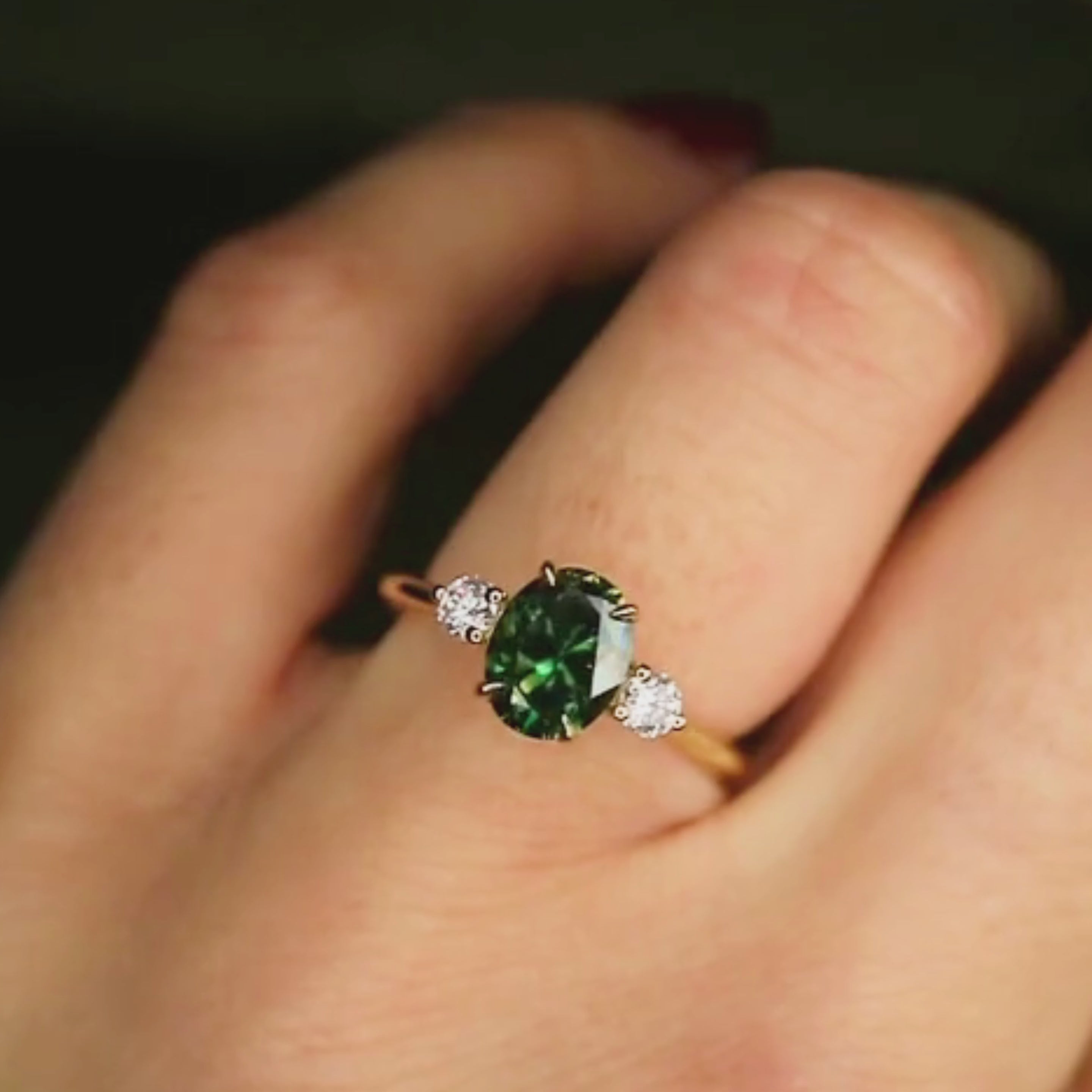 blue green oval trilogy sapphire engagement ring on hand in the light